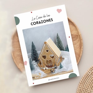 Puede incluir: Una casa de jengibre decorada con corazones y rodeada de árboles en miniatura cubiertos de nieve. La casa está etiquetada como "La Casa de los CORAZONES" y el texto "@letablierdechloe" está en la parte inferior de la imagen.