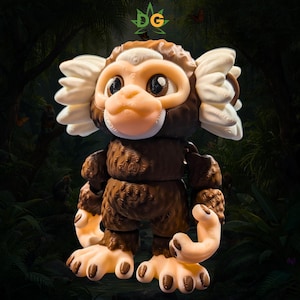 May include: A brown and cream-colored articulated monkey figurine with large dark eyes, prominent white ear tufts, and textured fur detailing. The figure features a light-colored face, hands, and feet, with the letters DG displayed at the top.