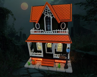 May include: A miniature Halloween-themed haunted house with an orange roof and black walls. The house features a white porch, windows with interior lights, and a spiderweb design. A pumpkin and address sign are in front of the house.