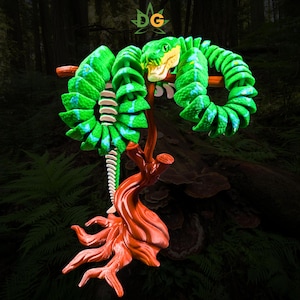 May include: A green articulated snake toy with blue accents coiled around a brown, textured tree branch stand. The snake features a detailed head with visible eyes and mouth, and the entire structure is supported by a base resembling tree roots.
