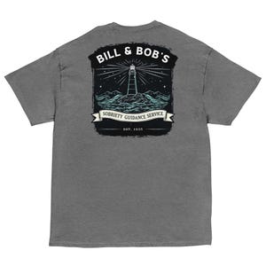 Puede incluir: Camiseta gris con un diseño de faro. El texto "BILL & BOB'S" está encima del faro, y "SOBRIETY GUIDANCE SERVICE" debajo. El diseño incluye un faro, olas y estrellas. También está presente el texto "EST. 1935".