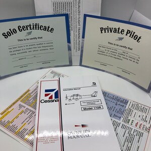 Puede incluir: Dos certificados azules y blancos para un piloto en solitario y un piloto privado. Los certificados tienen un pequeño icono de avión y el texto "Solo Certificate" y "Private Pilot". Un manual de avión Cessna 172R blanco con el texto "Owner's Manual" y "The Cessna Aircraft Company" está en primer plano.