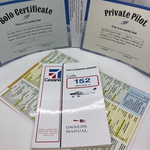 Puede incluir: Un manual de operación del piloto y un manual del propietario para un avión Cessna 152. La cubierta del libro es blanca con acentos rojos y azules. El título "Cessna 152" está impreso en negro sobre un fondo rojo. El libro está abierto a la sección del manual del propietario. La cubierta del manual es blanca con un diseño de bandera roja y azul. El texto "Manual del propietario" está impreso en negro sobre un fondo blanco.