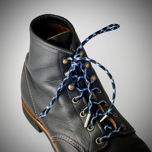 May include: Black leather work boots with blue and white striped laces. The laces are tied in a criss-cross pattern.