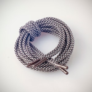 May include: Coiled black and white patterned shoelaces with metal aglets. The laces are patterned with a repeating diamond design. The shoelaces are on a white background.