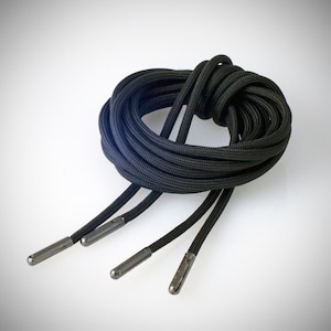 Könnte beinhalten: Schwarze Schnürsenkel mit silbernen Ösen. Die Schnürsenkel sind zusammengerollt.