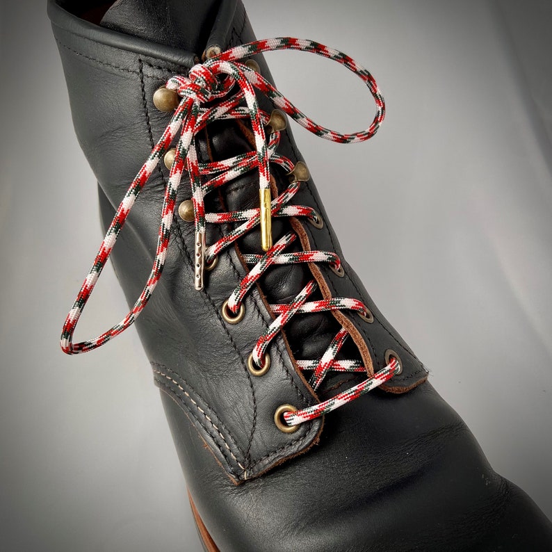 Puede incluir: Botas de cuero negro con cordones rojos, blancos y verdes. Los cordones est&aacute;n atados en un patr&oacute;n de cruz y asegurados con un cierre de metal dorado.