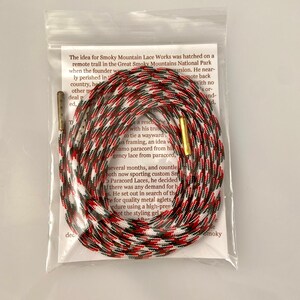 Puede incluir: Primer plano de una cuerda de paracord roja, blanca y negra con puntas de metal dorado. La cuerda est&aacute; enrollada y anudada. El texto "The idea for Smoky Mountain Lace Works was hatched on a remote trail in the Great Smoky Mountains National Park when the founder was on a solo excursion. He nearly perished in the wilderness, but he made it back with no injuries. He had a rescue rope with his trusty paracord to tie a wayward branch to his framing, an idea was born. Smoky Mountain Lace Works is a small business that makes custom paracord laces from paracord.  " es visible en el fondo.