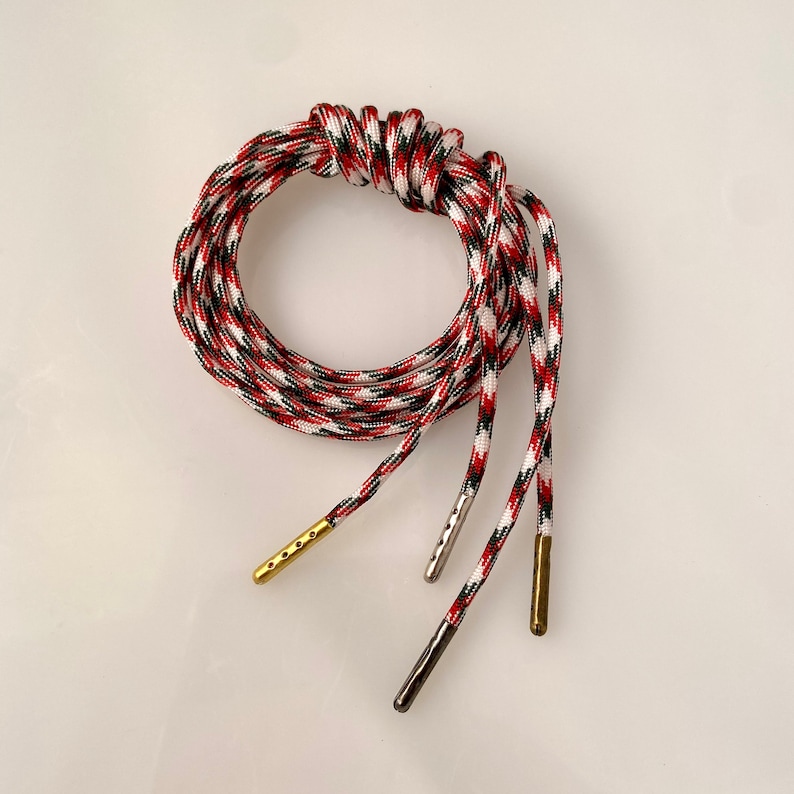 Puede incluir: Cord&oacute;n de paracord rojo, blanco y negro con aglets dorados y plateados.
