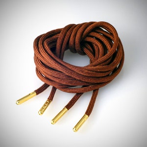 May include: Brown shoelaces with gold metal aglets. The shoelaces are coiled together.