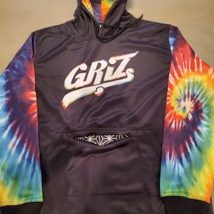 Op de afbeelding: Zwarte tie-dye hoodie met een wit "GRIZ" logo op de voorkant. De hoodie heeft een zwarte zak met een geometrisch patroon op de voorkant.
