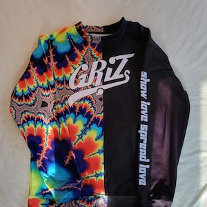 Puede incluir: Una sudadera negra y azul con un patrón psicodélico en un lado y negro en el otro. El lado negro tiene la palabra "GRiZ" en blanco y la frase "Show love Spread love" en blanco en la manga.