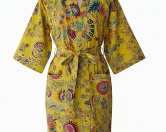 Puede incluir: Bata amarilla con estampado floral y cinturón a juego. La bata presenta un cuello en V, mangas tres cuartos y dos bolsillos delanteros. El estampado floral incluye detalles en rojo, azul y verde. La bata se exhibe en un maniquí.