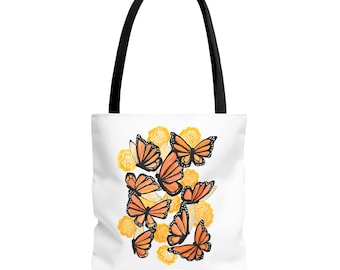 Puede incluir: Bolso tote blanco con asa negra, con un diseño de acuarela de mariposas monarca naranjas y negras y flores amarillas. El bolso está hecho de un material duradero y es adecuado para transportar varios artículos.