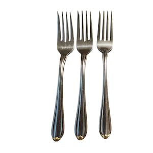 May include: Three silver forks with a classic design. Each fork has four tines and a handle that tapers to a rounded end with a gold-colored accent. The forks are arranged against a white background.