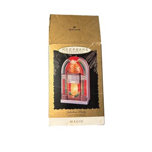 May include: A Hallmark Keepsake Ornament box featuring a jukebox design. The box is gold with a black and gold background. The ornament is a miniature jukebox with red, green, and yellow lights. The text on the box reads "Jukebox Party LIGHT AND MUSIC MAGIC."