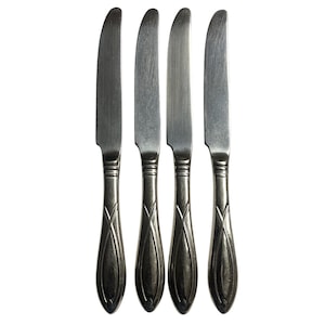 Puede incluir: Cuatro cuchillos de mesa de acero inoxidable con una hoja curva y un mango decorativo. Los mangos tienen forma ovalada con un diseño entrecruzado. Los cuchillos están dispuestos verticalmente sobre un fondo blanco.