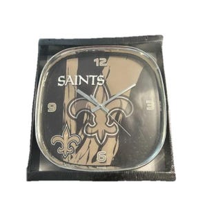 May include: Square clock with the word "SAINTS" in white lettering. The clock face features a fleur-de-lis emblem and a black and gold color scheme. The clock is in a black box.