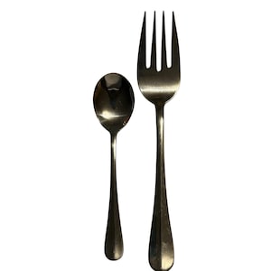 Puede incluir: Un juego de cuchara y tenedor de acero inoxidable. La cuchara tiene un cuenco redondeado y un mango largo y delgado. El tenedor tiene cuatro púas y un mango a juego. Ambas piezas son brillantes.