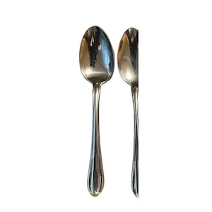 May include: Two silver spoons with elongated oval bowls and long, ridged handles. The spoons are displayed against a white background, showcasing their polished, reflective surfaces. The spoons are likely for serving or eating.