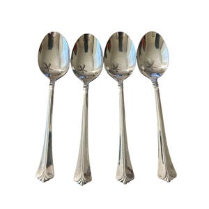 May include: A set of four polished silver-tone metal spoons arranged vertically. Each spoon features an oval bowl and a slender handle that widens toward the base, which is decorated with a subtle, fan-shaped embossed detail at the very end.