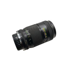 May include: A black camera lens with a textured grip and multiple adjustment rings. The lens has markings for distance in feet and meters, with a green and white label indicating the horizontal and vertical image size.