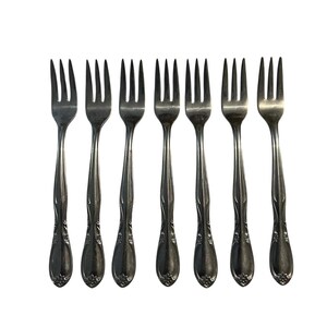 May include: A collection of seven silver forks, each featuring a decorative floral pattern on the handle. The forks, with four tines, are arranged in a row. Ideal for formal dining, they are set against a white backdrop.