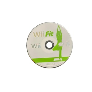 May include: A circular Wii Fit video game disc for the Nintendo Wii console. The disc features a white background with the text Wii Fit and Wii printed in green and grey. A green silhouette of a person performing a yoga pose is visible.