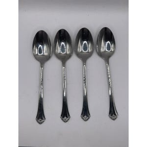 Puede incluir: Cuatro cucharas plateadas dispuestas en fila. Cada cuchara tiene un cuenco redondeado y un mango largo y delgado. Los mangos tienen un diseño decorativo cerca de la base y un diseño texturizado. Las cucharas son reflectantes.