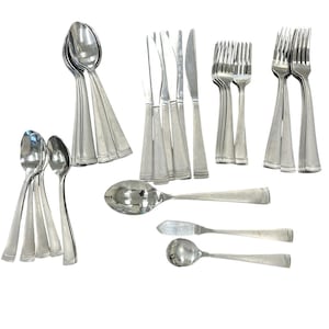 Pode incluir: Uma coleção de talheres de aço inoxidável, incluindo colheres, garfos, facas e facas de manteiga. Os talheres têm um design simples e elegante com um acabamento polido, adequado para refeições formais. A disposição mostra várias peças para uma mesa completa.