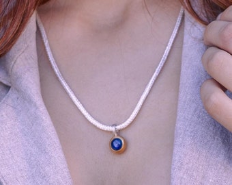 May include: A woman with long, red hair wearing a silver necklace with a blue gemstone pendant and matching earrings. She is also wearing a ring with a blue gemstone.