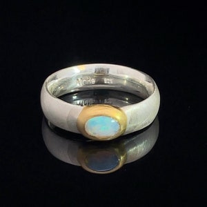 May include: A silver ring with a gold band and a white opal gemstone. The ring is marked "925" on the inside.