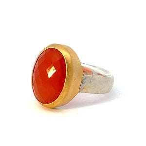 May include: A gold ring with a large, round, orange gemstone set in the center. The ring band is made of silver.