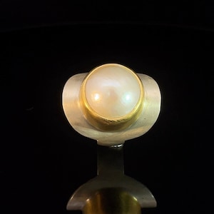 May include: A silver ring with a gold setting and a white pearl.