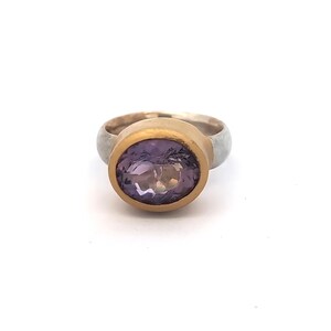 May include: A gold and silver ring with a large, oval-cut amethyst gemstone. The amethyst is a deep purple colour, set in a gold bezel. The ring's band is silver. A piece of jewellery.