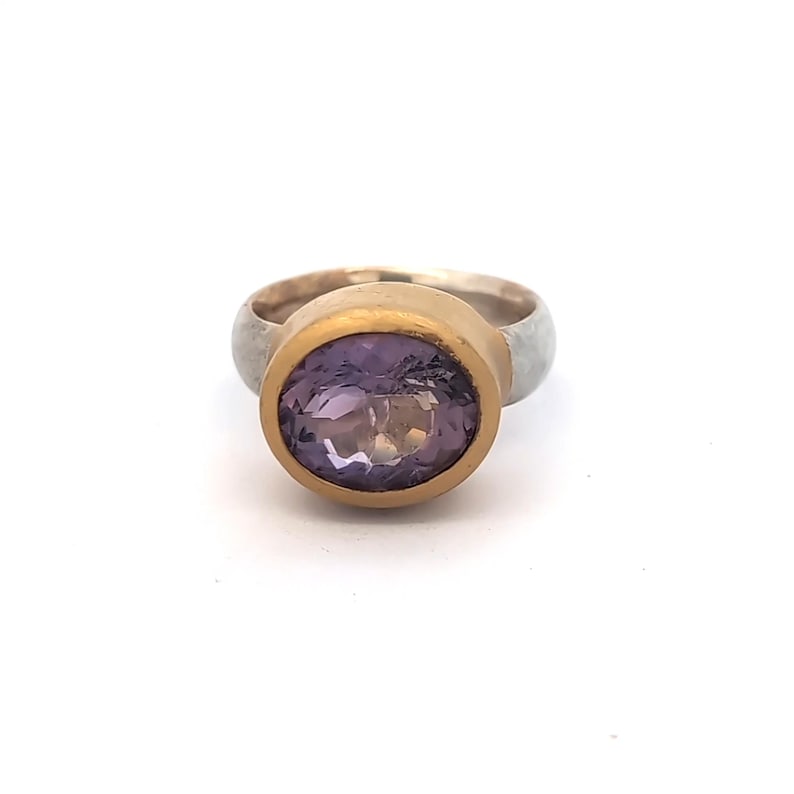 May include: A gold and silver ring with a large, oval-cut amethyst gemstone. The amethyst is a deep purple colour, set in a gold bezel. The ring's band is silver. A piece of jewellery.