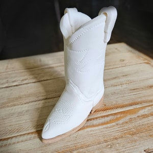 May include: A white cowboy boot with a pointed toe and a decorative pattern on the shaft.