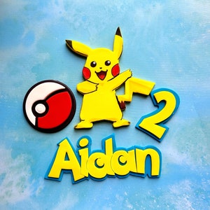 Op de afbeelding: Geel Pikachu-personage met een rode en witte Pok&eacute;bal, een geel nummer 2 en de naam Aidan in gele en blauwe letters.