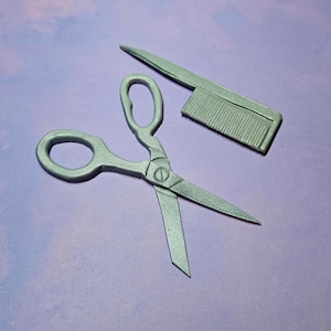 May include: A pair of silver scissors and a silver comb on a purple background.