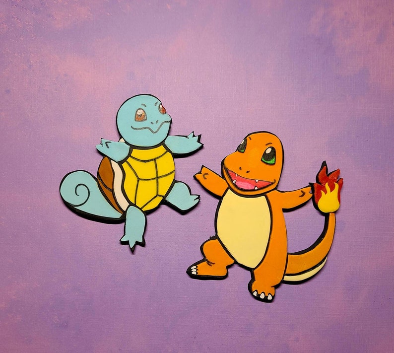 Op de afbeelding: Een blauwe en gele cartoon schildpad en een oranje cartoon hagedis met een vlammende staart. De schildpad heeft een schild met een geel midden en een blauw lichaam. De hagedis heeft een geel lichaam en een rode vlammende staart.