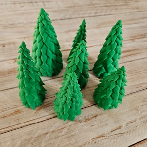 May include: Six green miniature pine trees made of a textured material, arranged in a circle on a wooden surface.