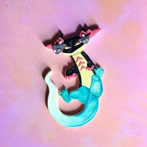 Op de afbeelding: Een zwarte en gele hagedis met een turquoise staart en roze accenten. De hagedis heeft drie ogen en een woeste uitdrukking.