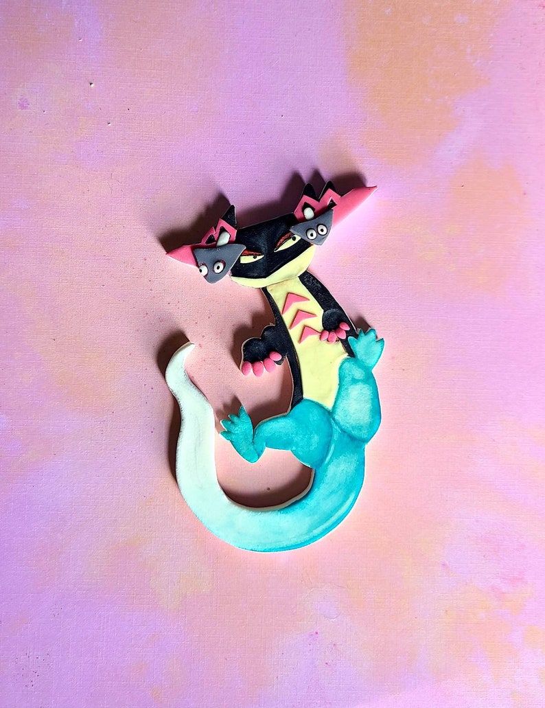 Op de afbeelding: Een zwarte en gele hagedis met een turquoise staart en roze accenten. De hagedis heeft drie ogen en een woeste uitdrukking.