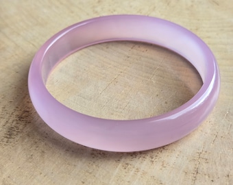 May include: A pale pink bangle bracelet made of smooth, polished stone. The bracelet is round and has a glossy finish.