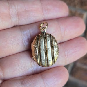 May include: A gold oval locket with engraved vertical lines and floral patterns. The locket has the initials "S R P" engraved on the front. It has a small loop at the top for a chain.