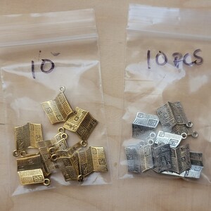 K&ouml;nnte beinhalten: Zwei Beutel mit 10 goldenen und silbernen Zeitungsanh&auml;nger. Die Anh&auml;nger sind in Form von gefalteten Zeitungen mit dem Aufdruck "City News" gestaltet.
