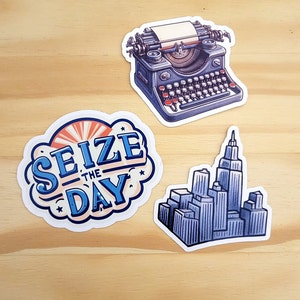 K&ouml;nnte beinhalten: Drei Aufkleber mit einer Vintage-Schreibmaschine, einer Skyline und einer blauen und wei&szlig;en Wolke mit dem Text "Nutze den Tag".