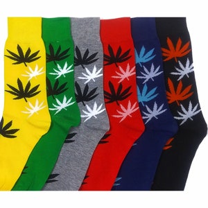 May include: A collection of seven colorful socks, each featuring a repeating pattern of cannabis leaves. The socks are in various colors, including yellow, green, gray, red, navy, and black, with the leaves in contrasting colors.