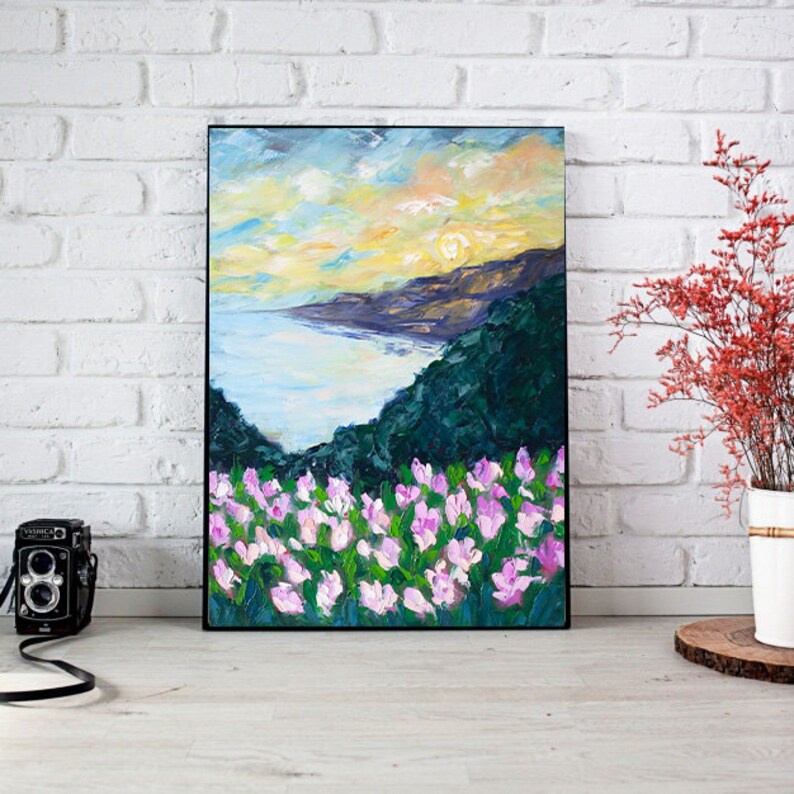 Puede incluir: Una pintura de un paisaje costero con una puesta de sol sobre el oc&eacute;ano. En primer plano, un campo de flores rosas.