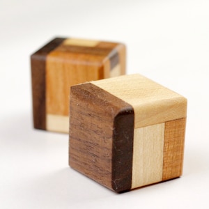 May include: Two wooden cubes with different wood grain patterns. The cubes are made of light and dark wood and have a natural finish.